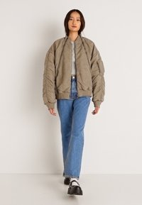 Przesadnie duża beżowa kurtka bomber z Ribbed mankietami i dołem, w połączeniu z jasnoniebieskimi dżinsami prostymi oraz czarnymi butami. Gładka tekstura i minimalistyczny design.