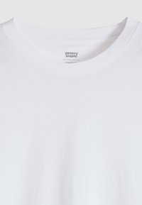 Λευκό T-shirt Levi’s με λαιμόκοψη crew neck που δείχνει το γιακά και μέρος της περιοχής του στήθους, το ύφασμα είναι λείο και απλό με ορατή ετικέτα του brand στο εσωτερικό του λαιμού.