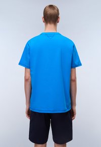 Modré tričko s krátkým rukávem a kulatým výstřihem, vyrobené z hladkého materiálu. Má rovný střih a jemný šev na zadní straně.