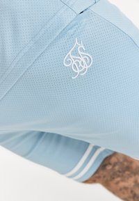 Shorts de sport bleu clair en tissu mesh, avec un logo brodé blanc et des rayures blanches le long de l'ourlet.
