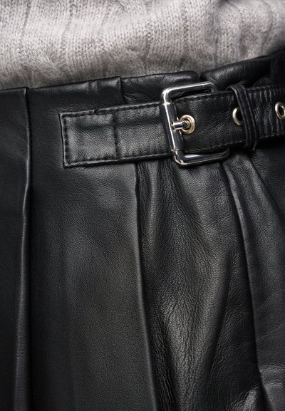 Jupe en cuir noir avec une ceinture à boucle argentée, associée à un pull en maille côtelée gris clair, rentré à la taille.