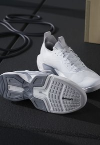 Coppia di scarpe sportive bianche su una superficie nera, una mostra la suola con motivo del battistrada grigio e bianco e marchio Continental.