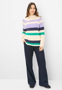 Gestreifter Pullover mit Mock-Neck; die Farben umfassen Lavendel, Marineblau, Creme und Grün. Kombiniert mit weiten Marineblau-Hosen und schwarzen Schuhen.