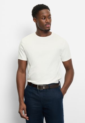 Weißes T-Shirt mit kurzen Ärmeln und Rundhalsausschnitt, kombiniert mit dunkelblauer Hose und braunem Gürtel. Der Stoff wirkt glatt und eng anliegend.