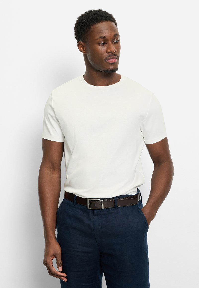 T-shirt blanc à manches courtes avec col rond, accompagné d'un pantalon bleu foncé et d'une ceinture marron. Le tissu semble lisse et ajusté.