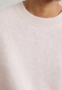 Maglione rosa chiaro realizzato in tessuto morbido e soffice. Presenta un collo a coste e una forma rilassata, evidenziando una superficie liscia e texurizzata.