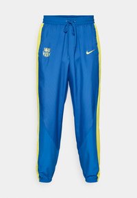 Niebieskie spodnie sportowe z żółtymi paskami po bokach. Posiadają elastyczny pas, ściągacz oraz logo drużyny piłkarskiej i Nike z przodu.