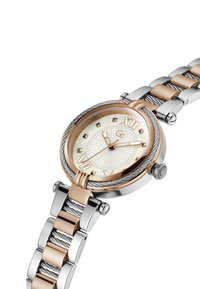 Montre ronde avec un boîtier en or rose, un cadran en nacre blanche, un bracelet en métal argenté et des chiffres romains en accents dorés.