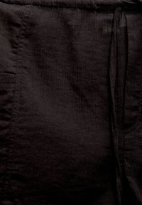 Tissu noir à texture travaillée, équipé d'une taille avec cordon de serrage et de poches latérales. Le matériau semble léger et légèrement froissé.