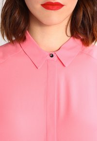 Rosa blus med en klassisk krage, svart knäppning och ett slätt, lätt tyger med en subtil lyster.