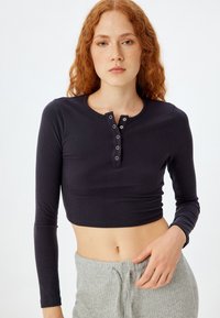 Marineblå ribbestrikket langærmet crop top med rund hals og knapdetalje. Stoffet er blødt, har en subtil tekstur og en tætsiddende silhuet.