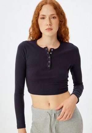 Marineblå ribbestrikket langærmet crop top med rund hals og knapdetalje. Stoffet er blødt, har en subtil tekstur og en tætsiddende silhuet.