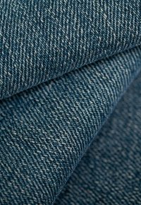 Tela de denim en varios tonos de azul con un notable patrón de sarga, presentando una superficie texturizada y sutiles variaciones en el color.