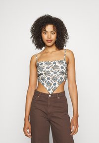 Top cropped com padrão floral em creme com detalhes em azul e castanho, apresentando um decote quadrado e bainha assimétrica, combinado com calças castanhas de cintura alta.