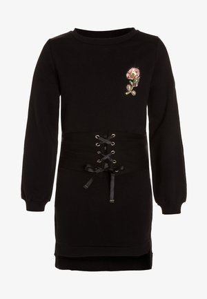 Sort kjole med lange ærmer med et pink blomstret patch på brystet og et bredt korsetlignende snørebælte i taljen.