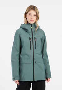 Grüne wasserdichte Jacke mit Kapuze, ausgestattet mit Reißverschlusstaschen, schwarzen Akzenten und einer lockeren Passform. Texturiertes Material für Langlebigkeit.