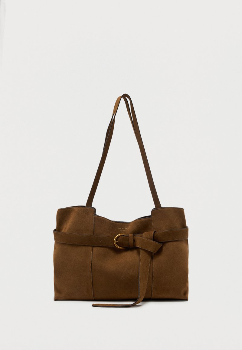 Καφέ τσάντα ώμου από σουέντ με μακριά λουριά και διακοσμητική ζώνη εμπρός με χρυσή αγκράφα, σε απλό φόντο.