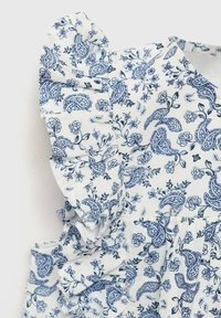 Bílá tkanina s modrými květinovými a paisley vzory. Obsahuje detaily s volánkovými rukávy. Měkká textura, lehký design vhodný pro teplé počasí.