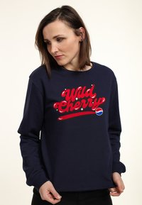 Felpa blu navy realizzata in misto cotone con testo grafico rosso in grassetto "Wild Cherry" e logo Pepsi. Maniche lunghe con polsini a coste.