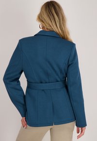 Teal blazer met riem, met een notch-kraag, gestructureerde schouders en schoudernaad; middelzwaar materiaal met een gladde textuur en een op maat gemaakte pasvorm.