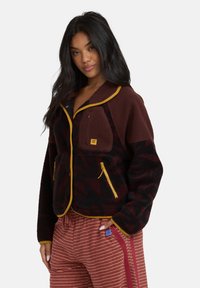 Polarowa kurtka w burgundowym i czarnym kolorze z żółtymi akcentami, z kołnierzem, kieszeniami na zamek i fakturowanym wzorem.