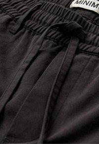 Gros plan d'un pantalon noir avec taille élastique, cordon de serrage et coutures visibles.