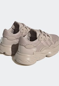 Ljust beige sneakers med nätmaterial och släta läderdetaljer. Rundad, texturerad sula med vågigt mönster. Har kontrasterande sömmar och öglor.