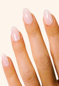 Uñas postizas con un degradado natural en tonos rosas, forma almendrada, acabado brillante. El tono de piel es claro con texturas visibles en los dedos.