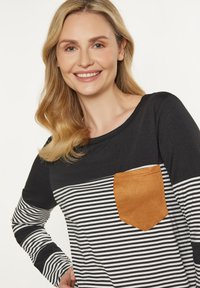 Langärmliges Hemd mit schwarzem und weißem Streifenmuster, das eine Tasche aus braunem Wildleder hat. Weicher Stoff und lässige Passform mit rundem Halsausschnitt.