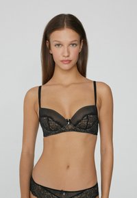 Czarny koronkowy biustonosz z głębokim dekoltem, regulowanymi ramiączkami i centralną dekoracyjną kokardą. Teksturowany w pasy i wzory kwiatowe.