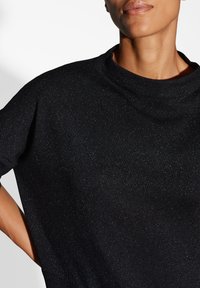 Haut tricot noir à col rond, présentant une texture scintillante subtile. Le design comprend une coupe ample et des manches courtes.