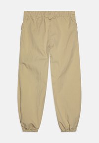 Lys beige elastiske bukser med avslappet passform, med samlede mansjetter og sidelommer. Glatt tekstur med minimal rynking.