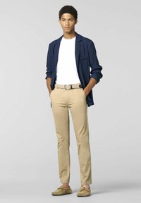 Navy patterned shirt over white t-shirt, khaki pants, beige belt, and light brown loafers. Model stands with hands in pockets against gray background.
