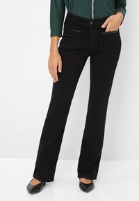 Jeans in denim neri con un design a gamba dritta, caratterizzati da tasche frontali con cuciture decorative, indossati con un top verde e ballerine nere.