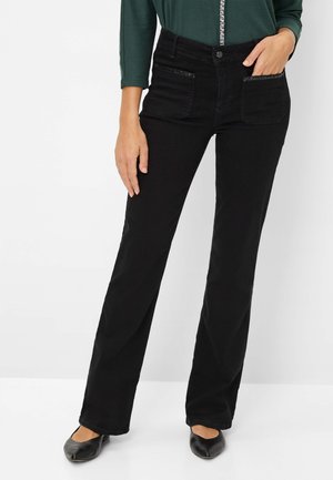 Schwarze Jeans aus Denim mit geradem Bein, mit Fronttaschen und dekorativen Stichen, getragen mit einem grünen Oberteil und schwarzen Ballerinas.