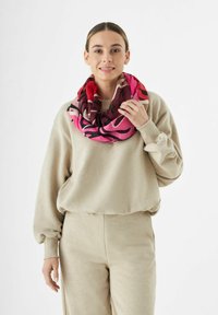 Écharpe imprimée colorée dans des tons de rose, bordeaux et noir, fabriquée en tissu doux, portée lâche autour du cou.