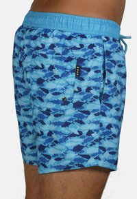 Shorts de bain arborant un imprimé camouflage bleu avec différentes nuances de bleu et des accents sombres. Taille élastique avec cordon de serrage et poche arrière.