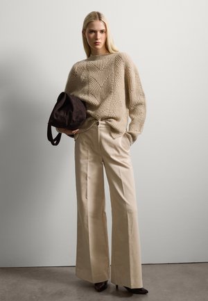 Jersey de punto beige con un patrón en forma de chevron; pantalones de pierna ancha crema; bolsa de hombro de ante marrón oscuro; tacones negros de punta.