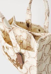 Leren schoudertas in crème met bruine patroon, voorzien van twee handvatten, binnenzakken, gouden hardware en een decoratief label.