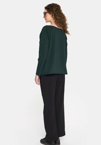 Zielona bluzka z długim rękawem o luźnym kroju, w zestawie z czarnymi spodniami o szerokich nogawkach. Teksturowany materiał, minimalistyczny design i okrągły dekolt.