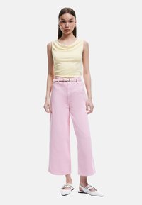 Top sin mangas de color amarillo claro combinado con pantalones anchos de cintura alta en color rosa y zapatos de punta blanca. Diseño minimalista con acentos de cinturón.