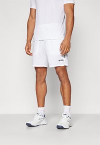 Shorts sportivi bianchi con il logo nero "BOSS" sul lato, abbinati a una t-shirt bianca e scarpe sportive bianche con accenti blu navy.
