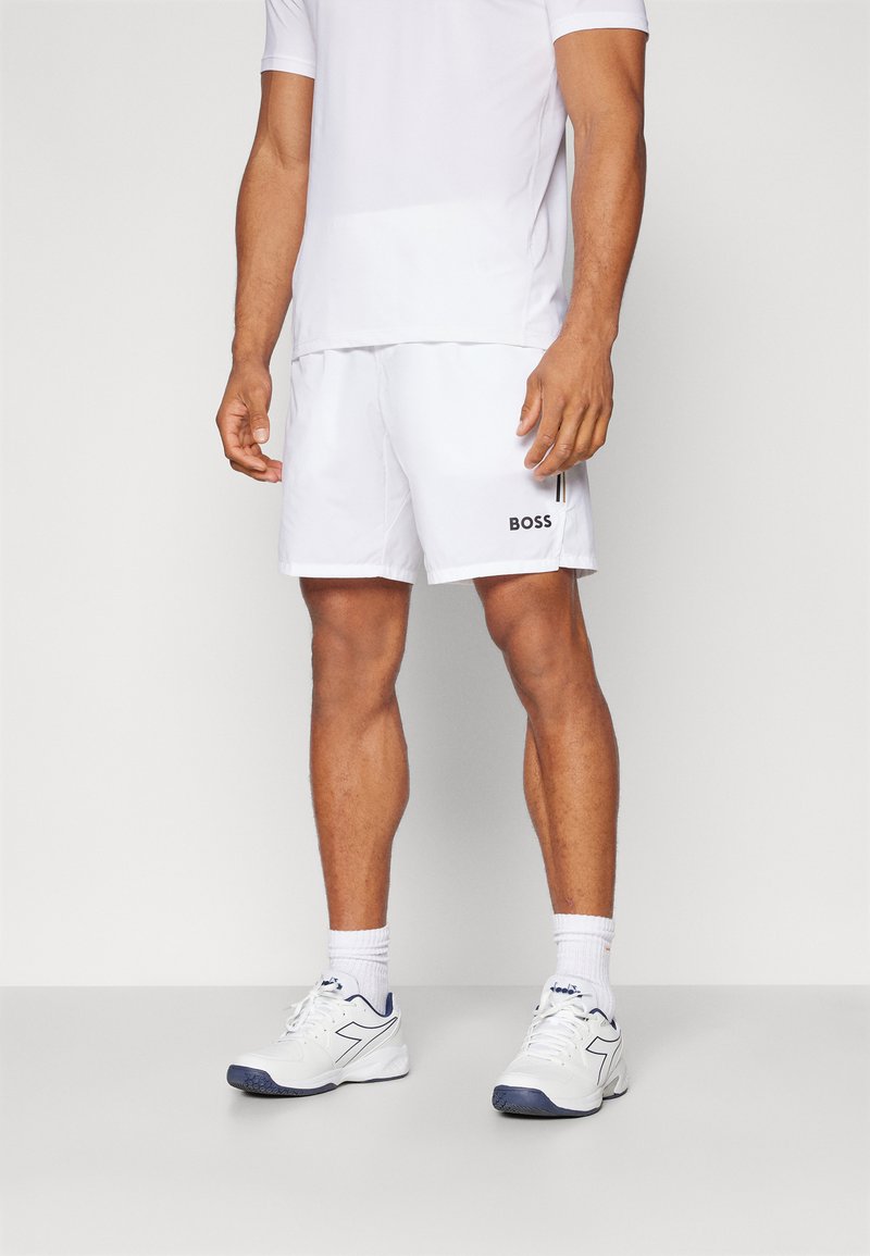 Shorts sportivi bianchi con il logo nero "BOSS" sul lato, abbinati a una t-shirt bianca e scarpe sportive bianche con accenti blu navy.