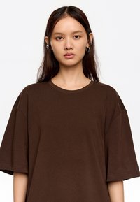 Brązowy oversize t-shirt wykonany z prążkowanej bawełny. Ma okrągły dekolt i krótkie rękawy, charakteryzuje się gładką teksturą oraz subtelnymi detalami w szwie.