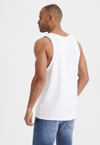 White sleeveless tank top made of cotton, featuring a round neckline and a relaxed fit. Paired with blue denim jeans.