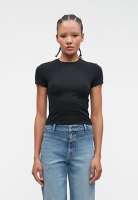 Czarna dopasowana koszulka z krótkimi rękawami, okrągłym dekoltem, w połączeniu z jasnoniebieskimi prostymi dżinsami z klasycznym pięciopocketowym krojem.