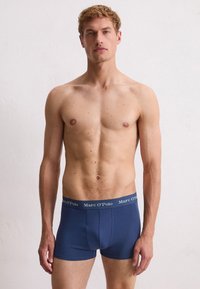 Granatowe szorty bokserskie wykonane z elastycznej tkaniny w jednolitym kolorze. Posiadają szary pas z brandingiem "Marc O'Polo" w białym tekście.