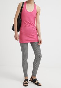 Fuksjowy top na ramiączkach zestawiony z legginsami w biało-czarny wzór w pied de poule. Czarna torebka przez ramię i płaskie sandały dopełniają strój.