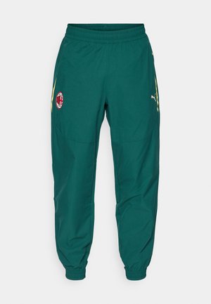 Zelene sportske hlače s rebrastim pojasom, zlatnim detaljima, bočnim džepovima i kružnim crvenim logom koji sadrži crno-bijeli emblem.