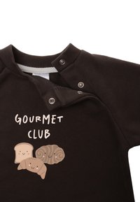 Brown cotton sweatshirt featuring snap buttons at the shoulder and a graphic print of bread and pastries with "GOURMET CLUB" text.
